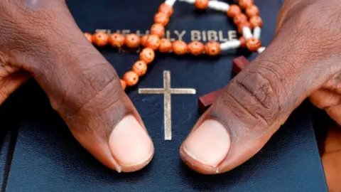 Getty Images Close-up of hands holding a bible and orange prayer beads